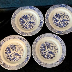 May include: Four white ceramic plates with a blue floral and bird design. Each plate has a detailed border and a central image of a bird and flowers. The plates are arranged on a dark surface.