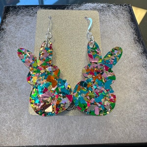 Może przedstawiać: Para kolorowych kolczyk&oacute;w w kształcie kr&oacute;lika wykonanych z mieniącego się brokatu. Kolczyki są srebrne i mają zwisający wz&oacute;r.