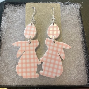 Puede incluir: Un par de pendientes de conejo de gingham rosa y blanco. Los pendientes est&aacute;n hechos de un material ligero y tienen un cierre de gancho plateado.