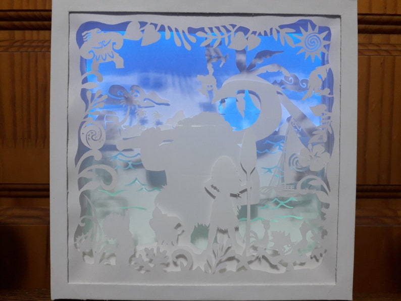 May include: A white, layered paper art piece depicting a tropical scene with a blue sky background. The artwork features silhouettes of characters, palm trees, a boat, and ocean waves, all within a white frame. The scene is illuminated with a blue light.