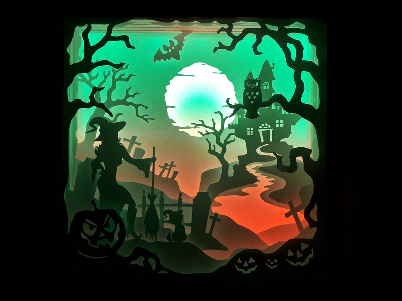 K&ouml;nnte beinhalten: Ein geschichtetes Papierkunstwerk, das eine Halloween-Szene darstellt. Silhouetten einer Hexe, eines Spukhauses, einer Eule und K&uuml;rbissen sind vor einem gr&uuml;n-orangen Farbverlaufshintergrund angeordnet. Ein Vollmond und unheimliche B&auml;ume vervollst&auml;ndigen das Design.