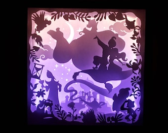 May include: A layered paper art piece depicting a scene from Aladdin. The artwork features silhouettes of characters, including Aladdin and Jasmine on a magic carpet, against a backdrop of a starry sky and a crescent moon. The color palette is primarily purple and white.