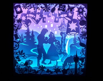 May include: A layered paper art piece depicting a romantic scene with silhouettes of a couple dancing, surrounded by floating lanterns, a tower, and a horse. The artwork features a color gradient of blue, purple, and white, creating a magical ambiance.