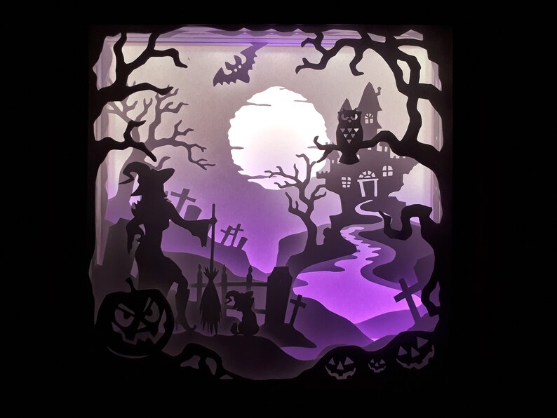 K&ouml;nnte beinhalten: Ein geschichtetes Papierkunstwerk, das eine Halloween-Szene darstellt. Eine Hexe, ein K&uuml;rbis und ein Spukhaus sind vor einem lila und wei&szlig;en Hintergrund silhouettenartig dargestellt. Ein Vollmond und eine Fledermaus sind ebenfalls zu sehen. Das Kunstwerk ist von innen beleuchtet.
