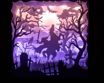 May include: A layered paper art piece depicting a spooky scene with a silhouetted rider on horseback, trees, tombstones, and bats. The artwork uses shades of purple and orange to create a dramatic, illuminated effect, perfect for Halloween.