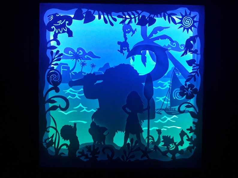 May include: A layered paper art piece featuring silhouettes of characters and scenes from a popular animated movie. The artwork depicts a tropical island setting with palm trees, ocean waves, and a sailboat, illuminated with blue and green light.