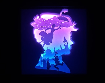 May include: A layered paper art piece featuring a silhouette of a woman with a hat and umbrella, with a cityscape and figures inside. The artwork uses shades of purple, blue, and white, creating a 3D effect against a black background.