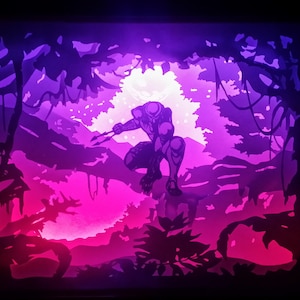 May include: A backlit art piece depicting a crouching figure in a jungle setting. The artwork uses shades of purple, pink, and black to create a dramatic scene. The figure is holding two spears, and the jungle foliage is silhouetted.