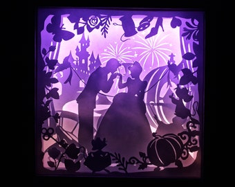 May include: A layered paper art piece illuminated with a purple glow, depicting a silhouette scene from a fairy tale. The artwork features a castle, fireworks, a horse-drawn carriage, and a couple in formal attire. Decorative elements include butterflies and floral accents.