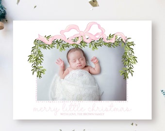 May include: A Christmas card with a pink bow and green garland. The card features a photo of a baby sleeping in a white blanket. The text on the card reads "merry little christmas" with "with love, the brown family" below.