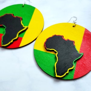 Puede incluir: Un par de pendientes grandes y redondos con un dise&ntilde;o colorido. Cada pendiente presenta una silueta negra del continente africano superpuesta a un fondo rojo, amarillo y verde. Los pendientes tienen ganchos plateados.