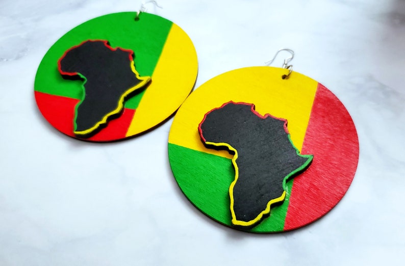 Puede incluir: Un par de pendientes grandes y redondos con un dise&ntilde;o colorido. Cada pendiente presenta una silueta negra del continente africano superpuesta a un fondo rojo, amarillo y verde. Los pendientes tienen ganchos plateados.