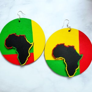 Puede incluir: Un par de pendientes grandes y redondos con una combinaci&oacute;n de colores vibrantes. Cada pendiente presenta una silueta negra del continente africano, delineada en amarillo y rojo, sobre un fondo verde, amarillo y rojo. Los pendientes tienen ganchos plateados.