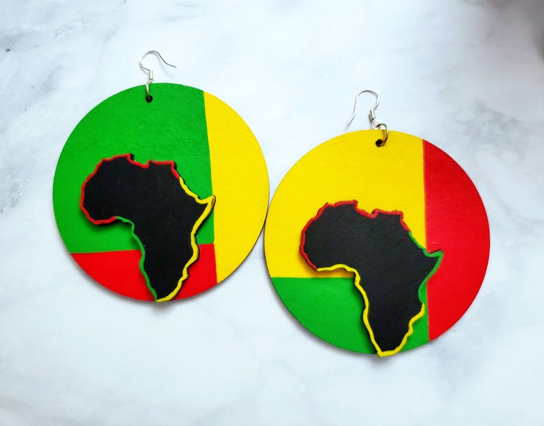 Puede incluir: Un par de pendientes grandes y redondos con una combinaci&oacute;n de colores vibrantes. Cada pendiente presenta una silueta negra del continente africano, delineada en amarillo y rojo, sobre un fondo verde, amarillo y rojo. Los pendientes tienen ganchos plateados.