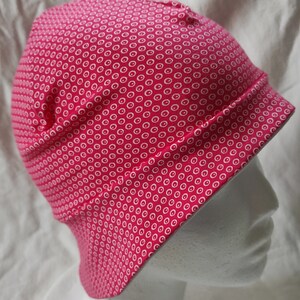 Könnte beinhalten: Eine rosa Mütze mit einem weißen Kreis-Muster. Die Mütze ist aus weichem, dehnbarem Stoff und hat eine lockere Passform.