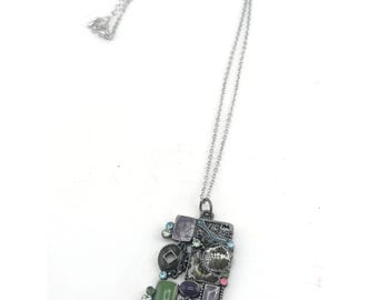 May include: Silver-tone necklace with a rectangular pendant. The pendant is adorned with an assortment of colorful gemstones in shades of green, purple, pink, and blue. The necklace is displayed against a white background.