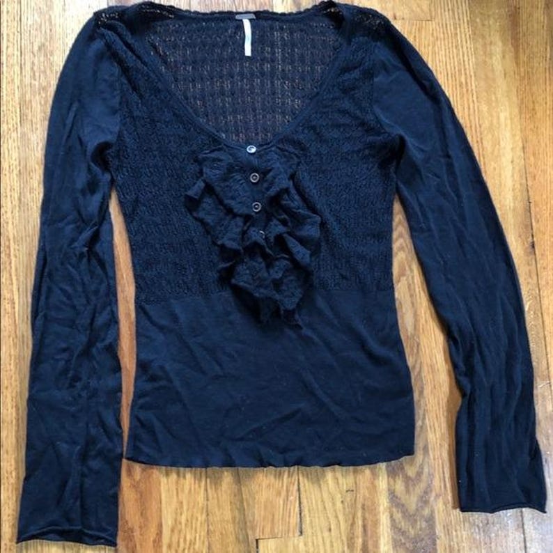 Pu&ograve; includere: Top nero a maniche lunghe con scollo a V e parte anteriore a balze. Il top presenta un corpetto in maglia strutturata e una sezione inferiore in tessuto liscio. L'etichetta del marchio &egrave; visibile allo scollo. Un capo versatile.