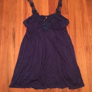 Puede incluir: Vestido azul oscuro con una silueta fluida. El vestido presenta intrincadas correas trenzadas y un adorno decorativo en el escote. La tela parece suave y cae suelta, creando un aspecto relajado y c&oacute;modo. El vestido es adecuado para ropa informal.