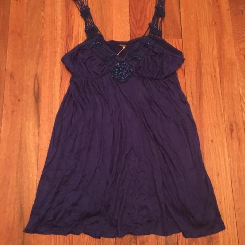 Puede incluir: Vestido azul oscuro con una silueta fluida. El vestido presenta intrincadas correas trenzadas y un adorno decorativo en el escote. La tela parece suave y cae suelta, creando un aspecto relajado y c&oacute;modo. El vestido es adecuado para ropa informal.