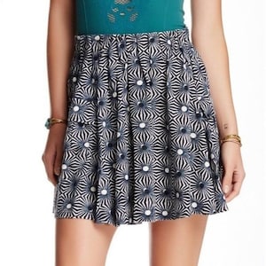 May include: A navy blue and white patterned mini skirt. The skirt features a repeating geometric design with white circles and radiating lines. The skirt is pleated and has a high waist. The fabric appears to be lightweight and suitable for warm weather.