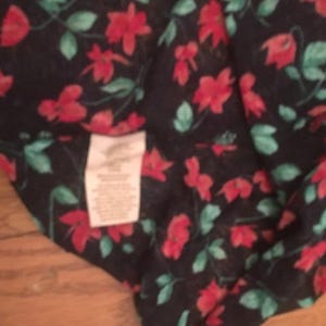 Puede incluir: Tela azul marino oscuro con un estampado floral rojo y hojas verdes. La tela tiene una etiqueta con texto. El dise&ntilde;o floral se repite en todo el material. La tela probablemente se utiliza para ropa o decoraci&oacute;n del hogar.