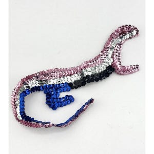 Könnte beinhalten: Eine Paillettenapplikation in Form eines Fisches mit rosa, weißen, schwarzen und blauen Pailletten.