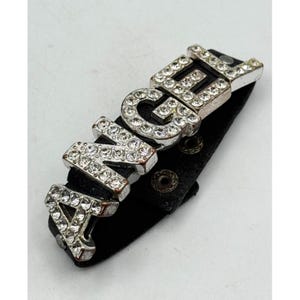 May include: A black leather bracelet with the word "ANGEL" spelled out in silver-toned metal letters encrusted with clear rhinestones. The bracelet has a snap closure.