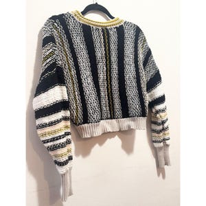 Puede incluir: Un su&eacute;ter a rayas corto con mangas largas. El su&eacute;ter es negro, blanco y amarillo. Las mangas tienen un patr&oacute;n de rayas multicolores.