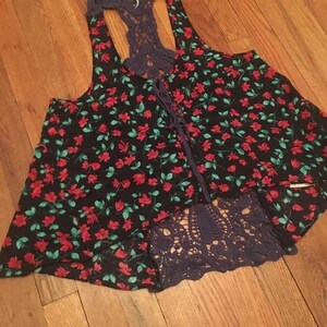 Puede incluir: Camiseta sin mangas negra con estampado floral rojo y hojas verdes. La parte superior presenta una espalda y un ribete de ganchillo azul marino, con cordones en la parte delantera. El dobladillo inferior tambi&eacute;n es de ganchillo azul marino.