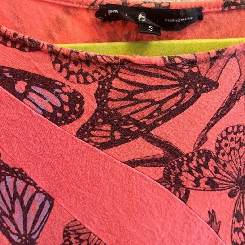 May include: Coral-colored top with a butterfly pattern in dark brown and purple. The top features a wrap-style design and a scoop neckline. The tag reads "People's Market".