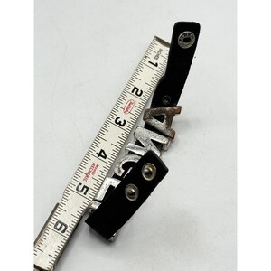 May include: Black leather bracelet with silver-toned metal letters spelling "ANGEL". The bracelet is measured with a white and red measuring tape. The bracelet is approximately 5 inches long.