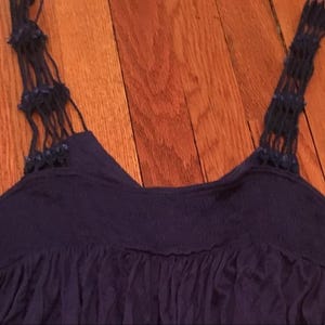 Puede incluir: Camiseta sin mangas azul marino con intrincadas correas de macram&eacute; azul oscuro. La parte superior presenta un dise&ntilde;o fruncido y fluido en el escote y una tela ligeramente texturizada. Las correas est&aacute;n adornadas con peque&ntilde;as cuentas azul oscuro.