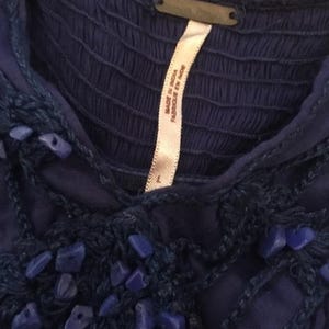 Puede incluir: Primer plano de un top azul oscuro con un corpi&ntilde;o texturizado y detalles decorativos de piedras azules. Una etiqueta blanca dice "Made in India Fabriqu&eacute; en Inde" y la talla es "L". El top es probablemente de estilo bohemio.