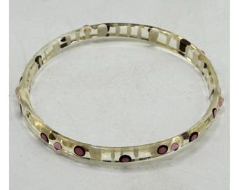 May include: A clear, round bangle bracelet with a light yellow tint. The bracelet is decorated with small, dark pink and brown circular accents. The design is simple and elegant, suitable for everyday wear.