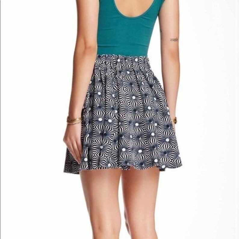 May include: A teal-colored tank top paired with a flared mini skirt. The skirt features a repeating pattern of navy blue and white starburst designs. The outfit is worn by a person.