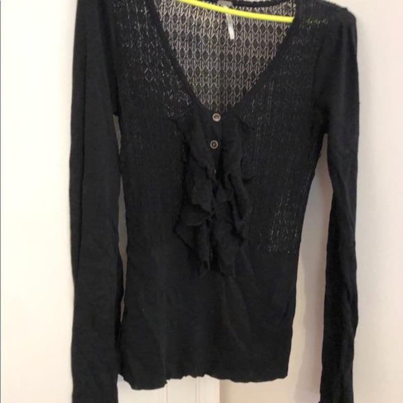 Pu&ograve; includere: Camicia nera a maniche lunghe con scollo a V e parte anteriore a balze. La parte superiore del petto presenta un motivo a maglia aperta e si chiude con due bottoni. Le maniche sono lunghe e aderenti.