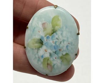 May include: Oval porcelain brooch with a hand-painted design of blue and white flowers on a light blue background.