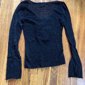Pu&ograve; includere: Top nero a maniche lunghe con scollo a V e maniche svasate. Il top &egrave; realizzato in tessuto a maglia e ha un corpetto aderente. Le maniche sono lunghe e a forma di campana, appoggiato su una superficie di legno.