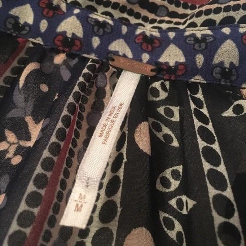 Op de afbeelding: Close-up van een top met patroon met een blauwe kraag en een label met de tekst "Free People". De stof heeft een mix van zwarte, beige en rode patronen. Het label zegt ook "Made in India / Fabriqu&eacute; en Inde".