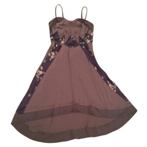 May include: A mauve-colored dress with thin straps and a flowing skirt. The dress features dark purple panels with floral patterns along the sides and bodice. The fabric has a satin-like sheen, giving it a luxurious appearance.