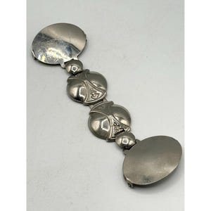 Könnte beinhalten: Eine silberfarbene Metallkette mit einer Reihe runder, dekorativer Glieder. Die Glieder haben ein erhabenes, strukturiertes Design.