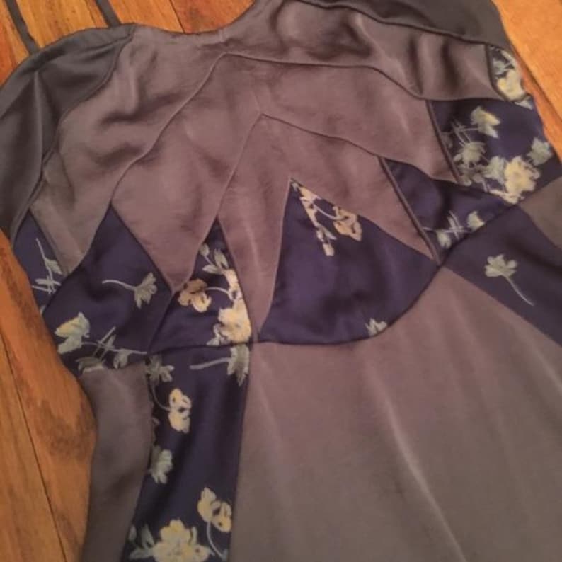 May include: A sleeveless top in shades of gray and purple, with a floral pattern in navy blue. The fabric appears to be a soft, silky material. The top has a unique, geometric design.