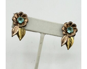 Könnte beinhalten: Ein Paar Vintage-Blumenohrringe. Jeder Ohrring hat eine kupferfarbene Blume mit einem hellblauen Mittelstein und zwei goldfarbenen Blättern. Die Ohrringe werden auf einem weißen Ohrringständer präsentiert.