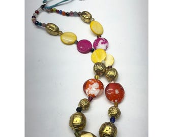May include: A colorful necklace featuring a variety of beads in gold, yellow, pink, and red. The necklace includes round, oval, and geometric shapes, strung on a teal cord with a silver clasp. The beads have a mix of textures and patterns.