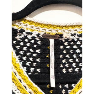 Puede incluir: Su&eacute;ter de crochet negro, blanco y amarillo con una etiqueta de Free People. La etiqueta dice "Knit in Taiwan, Finished in China" y "Tricote dans Taiwan, Fini en Chine".