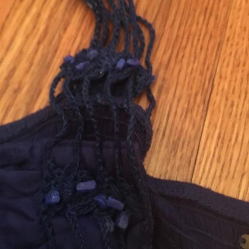 Puede incluir: Primer plano de un top azul oscuro con un dise&ntilde;o de correas tejidas. Las correas est&aacute;n adornadas con peque&ntilde;as cuentas azul claro. La tela parece ser un material suave y fluido. El top es probablemente una prenda de verano.