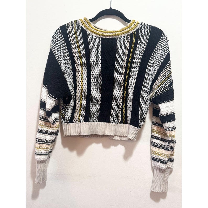 Puede incluir: Un su&eacute;ter corto a rayas con mangas largas. El su&eacute;ter es negro, blanco y amarillo.