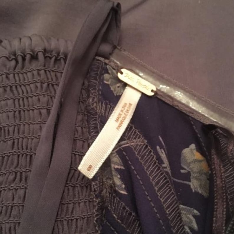 May include: Close-up of a dark gray dress with a textured bodice and a floral patterned lining. The dress has a tag that reads "Free People" and "Made in China, Fabriqu&eacute; en Chine". The size tag reads "8".