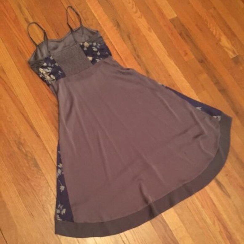 May include: A sleeveless dress with spaghetti straps, featuring a mauve skirt and a gray bodice. The bodice has floral patterned panels. The dress has a dark gray hem and dark blue floral accents on the sides.