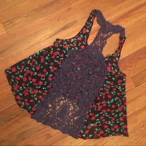 Puede incluir: Una camiseta sin mangas con estampado floral y espalda de crochet azul marino. El estampado floral presenta flores rojas y hojas verdes sobre un fondo negro. La espalda de crochet tiene un dise&ntilde;o calado detallado.